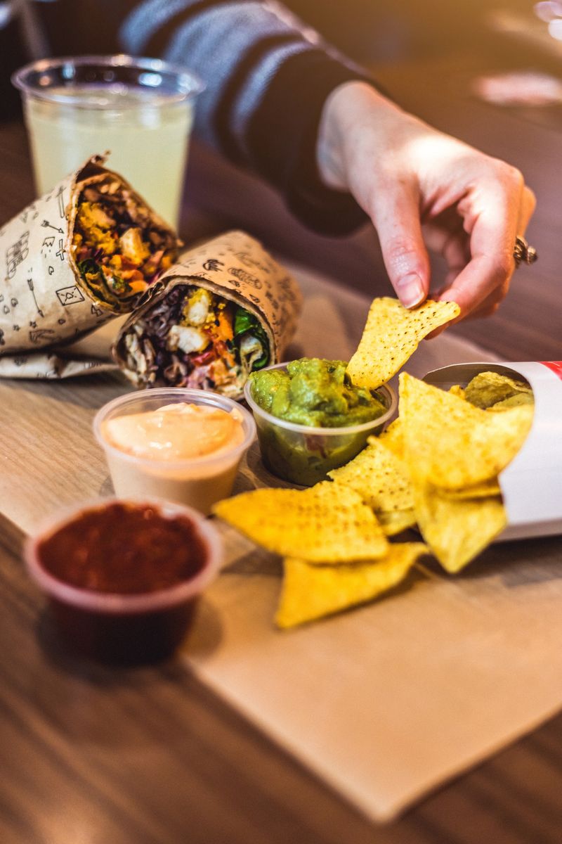 Nachos com guacamole e molhos ao lado de um burrito